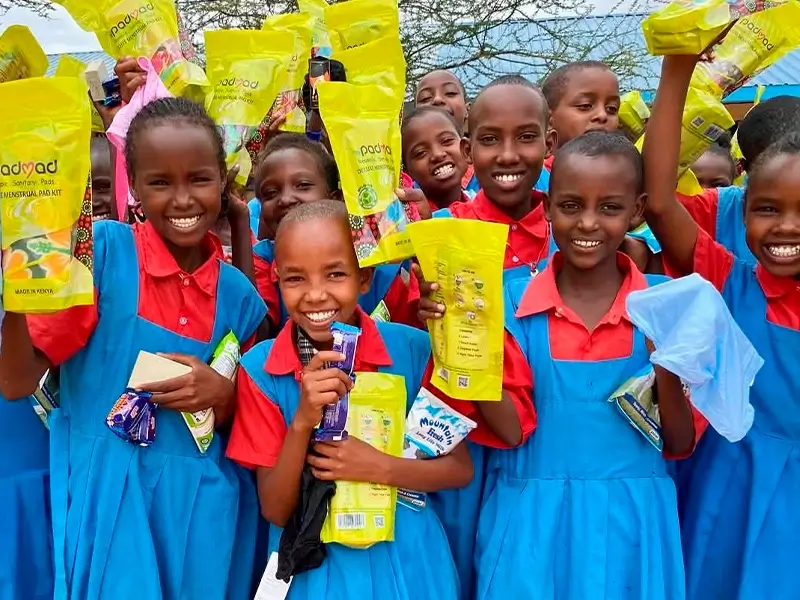A group of happy young girls and adolescents in Kenya smiling while holding their PadMad reusable sanitary pad packages after a community workshop to end period poverty