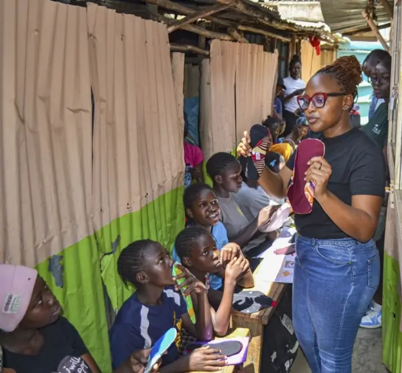 Padmad educator demonstrating reusable pads to smiling girls in a school
