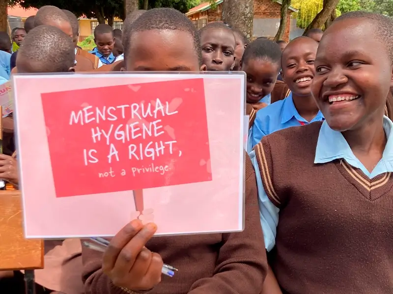 A group of smiling schoolgirls in Kenya; one of them holds a handmade sign that reads: 'Menstrual hygiene is a right! Not a privilege.