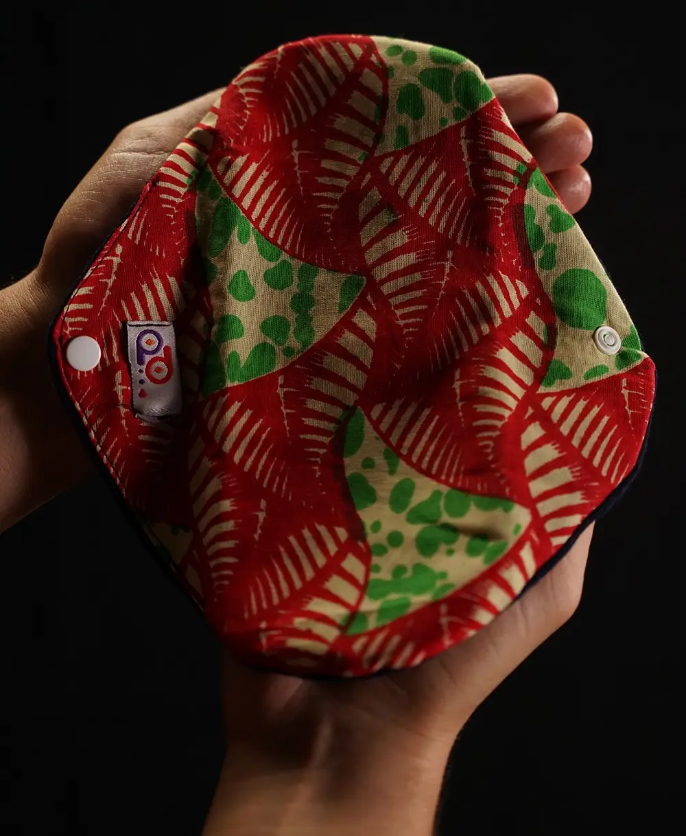A woman holding a PadMad pantyliner holder in her hands to demonstrate its compact size and portable design, featuring a bright, colorful pattern.